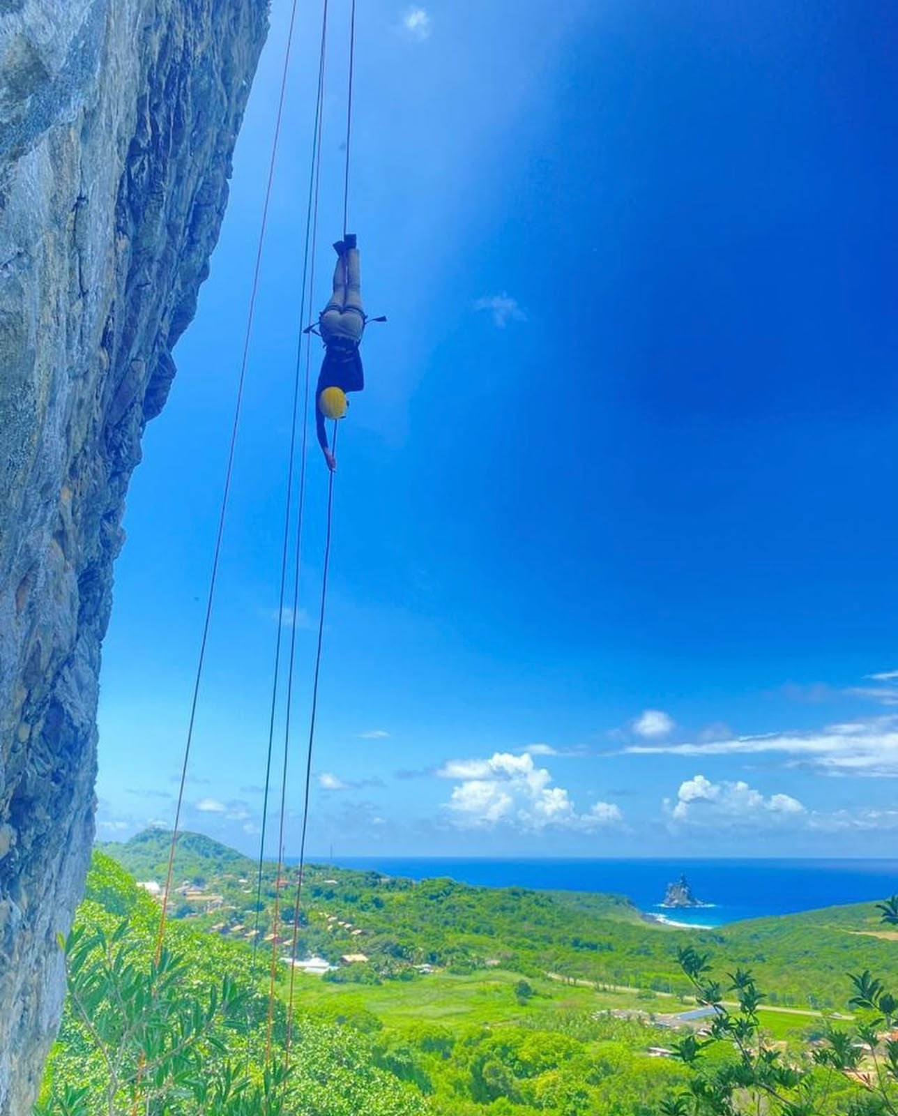 Pessoa descendo de rapel sobre a vegetação da ilha com o mar ao fundo