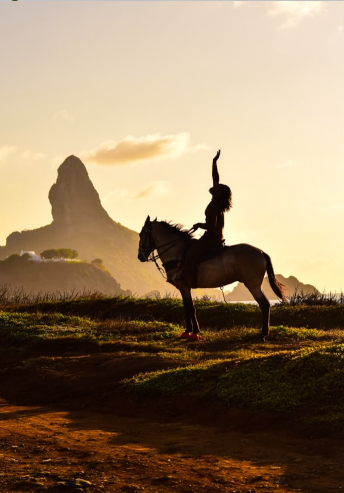 Cavaleiro levantando a mão a cavalo ao pôr do sol, com o Morro do Pico ao fundo
