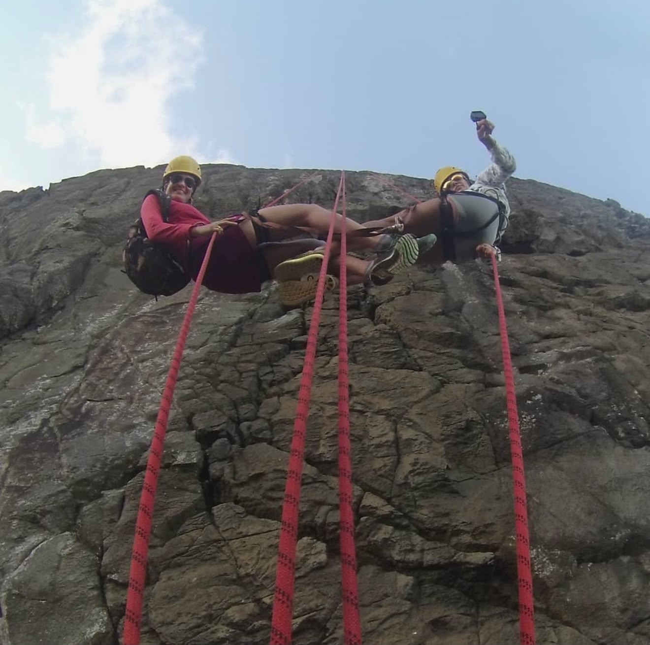Duas pessoas em rapel descendo a parede rochosa pelas cordas vermelhas