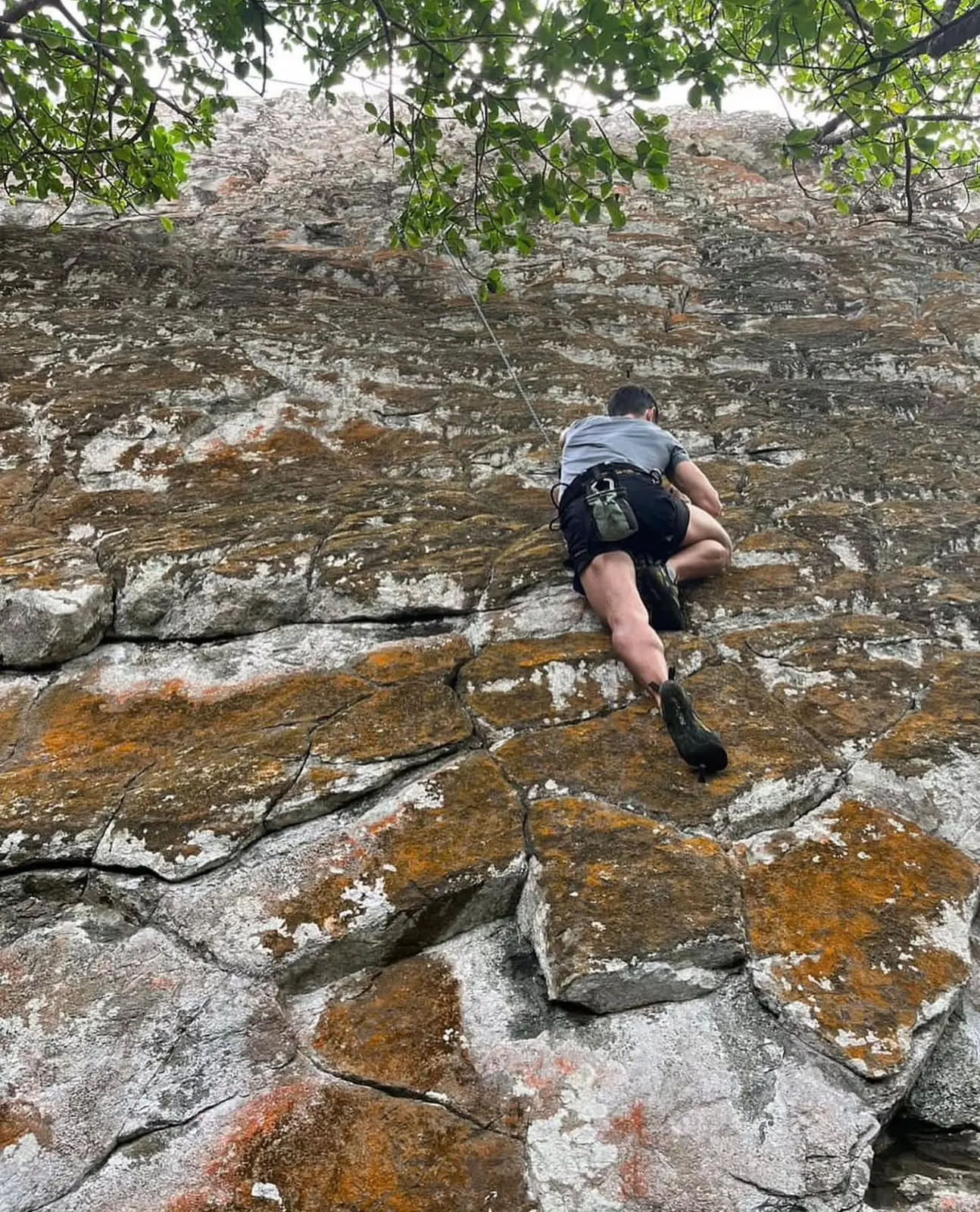Alpinista subindo a parede de pedra coberta de liquens do Piquinho